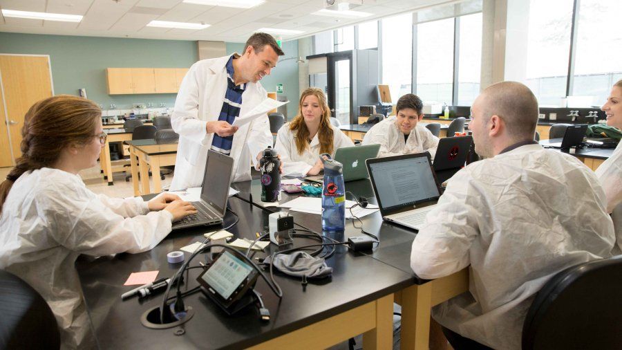 science professor and students all wearing white lab coats discussing a topic in a laboratory 