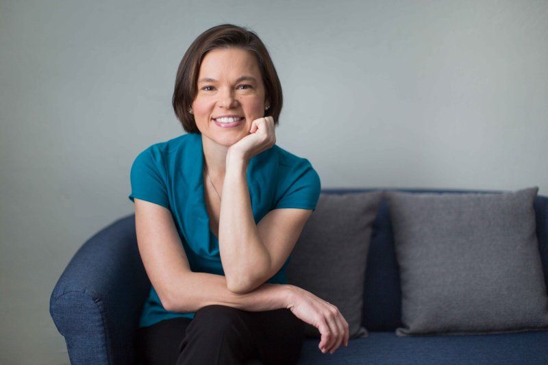 A counselor looks and smiles while sitting on a blue couch